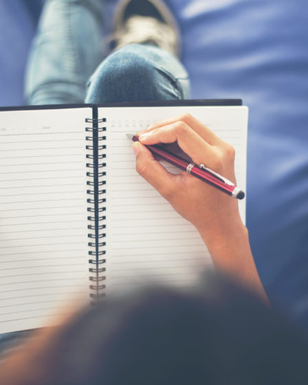 Woman hands writing on notepad lying at home