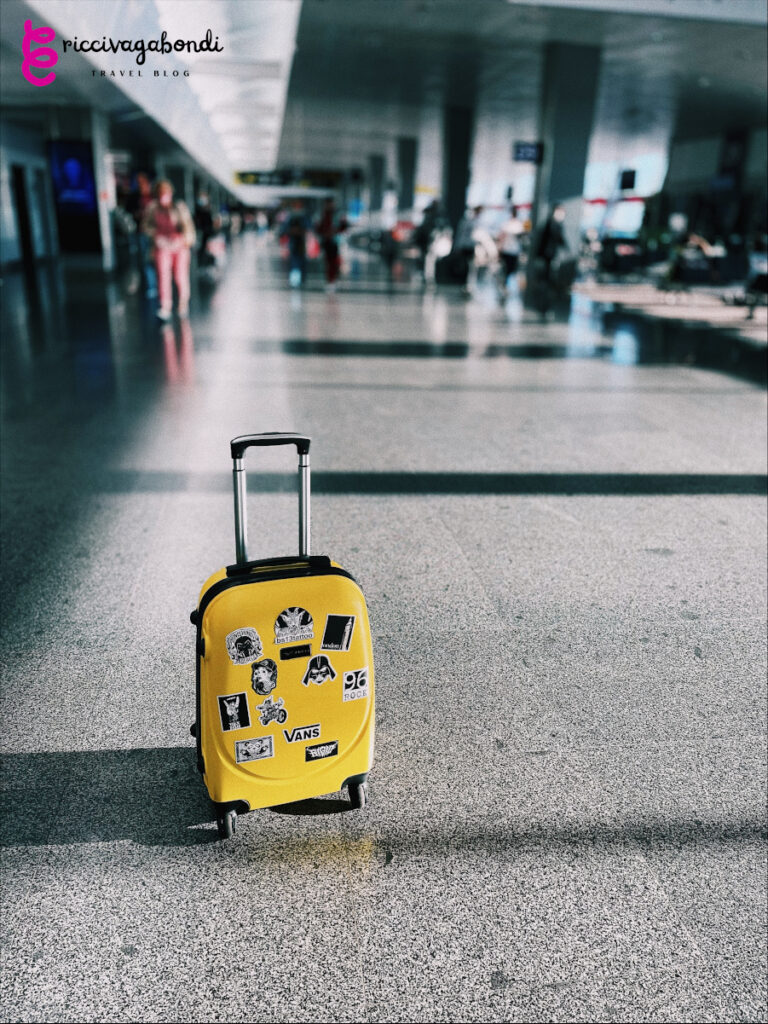 Yellow luggage with stickers at the station waiting to be picked up.